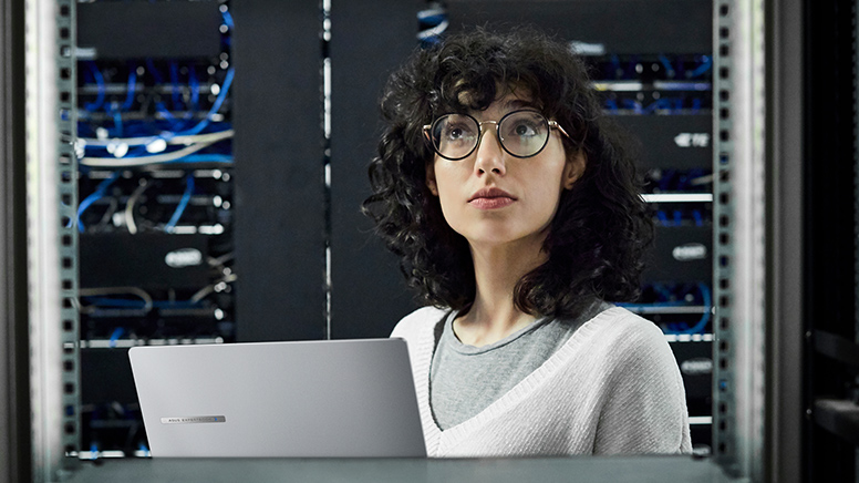 一名女性 IT 员工在服务器机房内，手上拿着 ASUS ExpertBook